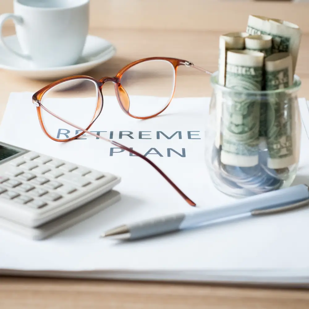 Retirement plan with calculator, glasses, and glass jars with dollars on top of it