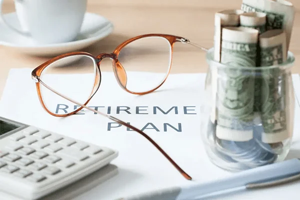 Retirement plan with calculator, glasses, and glass jars with dollars on top of it